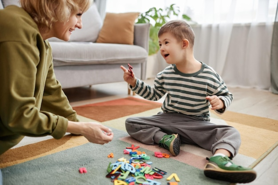 Happy little boy with Down syndrome playing on the floor with his mother