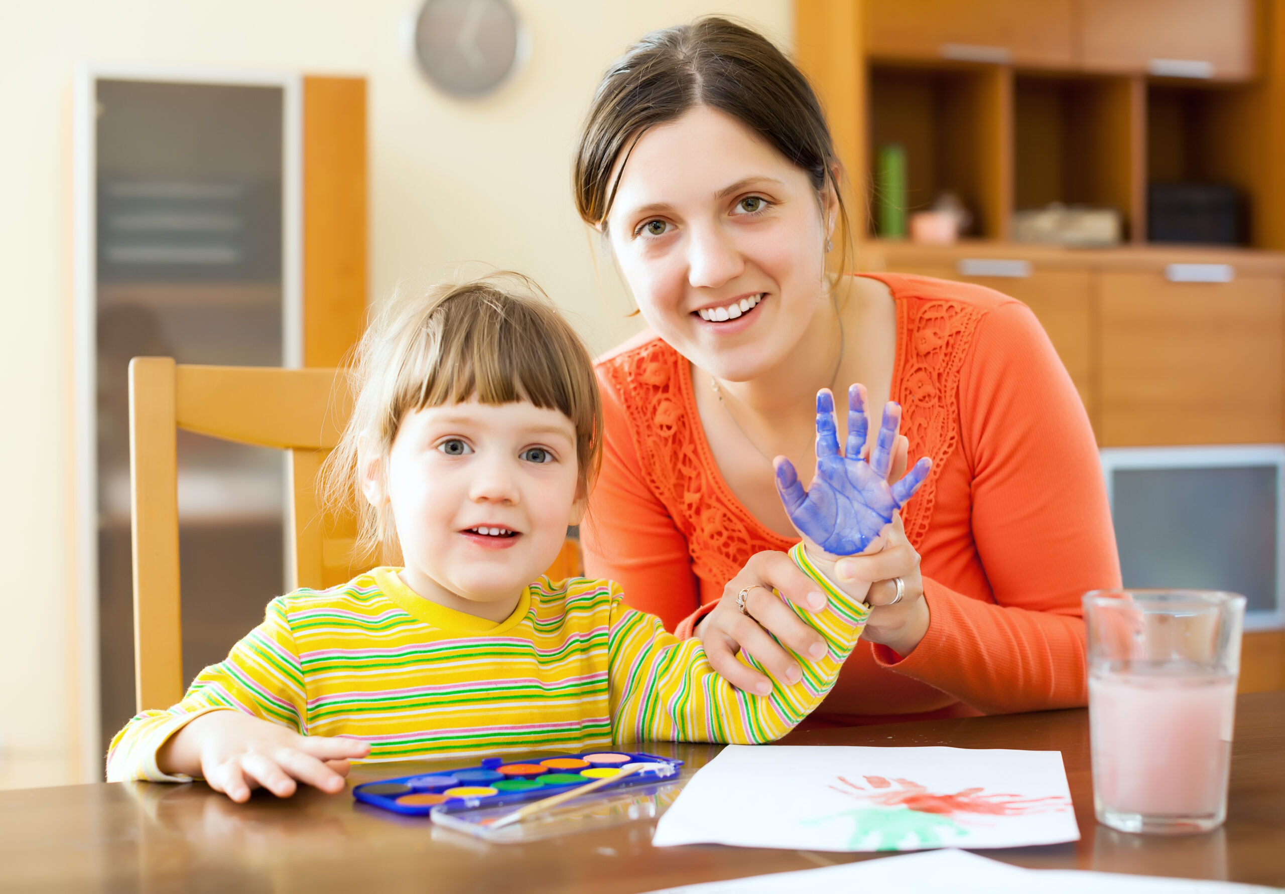 A mother and child happily painting together on paper at a table.