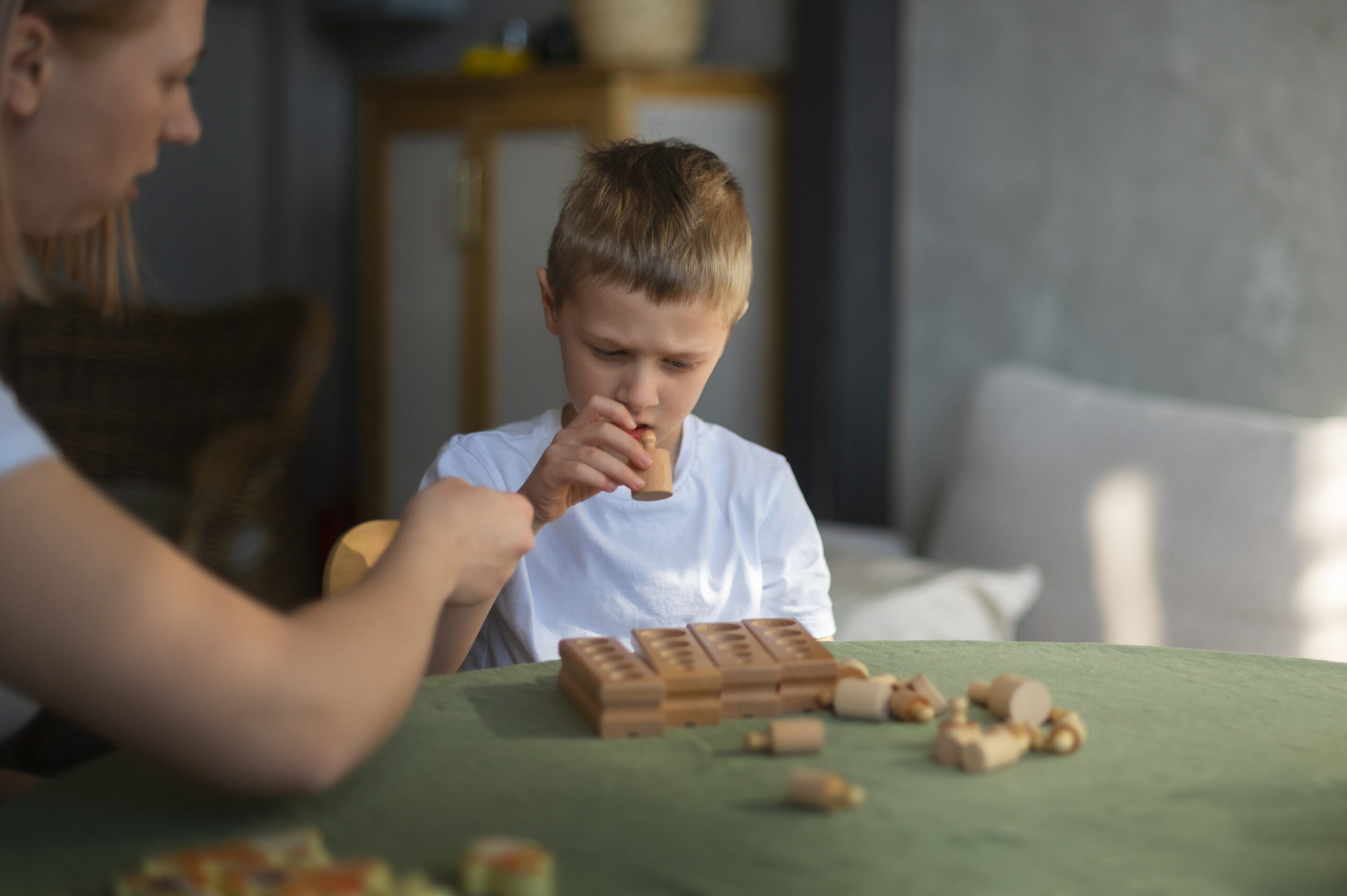 A mother playing with her autistic son on a carpet with toys.